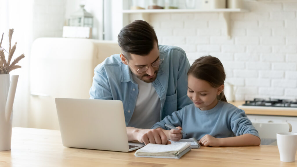 Caring young dad helping small primary pupil kid daughter preparing school homework, sitting together at table. Happy little child girl involved in doing task, studying homeschooling with father.
